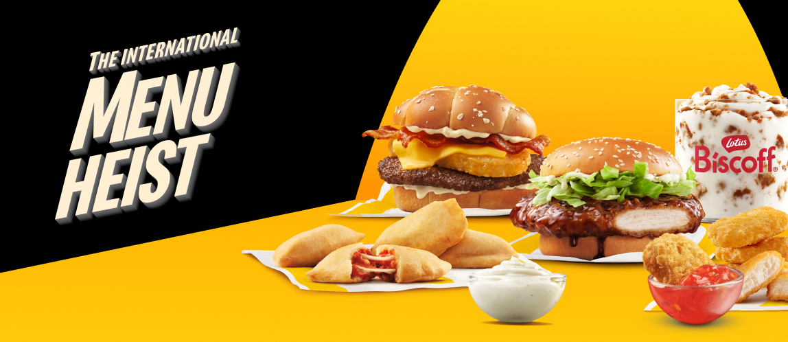 A spotlight illuminating a series of international McDonald’s menu items including a Big Rösti Burger, a Chicken Teriyaki Sandwich, a Biscoff® McFlurry®, McPizza Bites, McNuggets, a Garlic Mayo-Style Sauce, and a Sweet Tangy Chili Dip. Next to them are the words “The International Menu Heist”. 