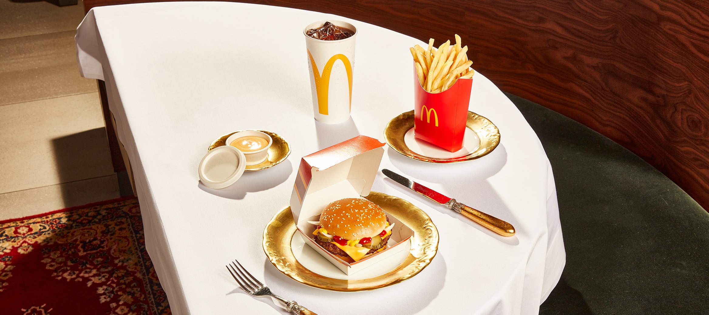 Wir sehen einen mit Gold gedeckten Tisch, auf dem das exklusive McMenü® mit Hamburger Royal Cheese, Pommes, Cola und limitiertem Cheese Dip angerichtet ist.