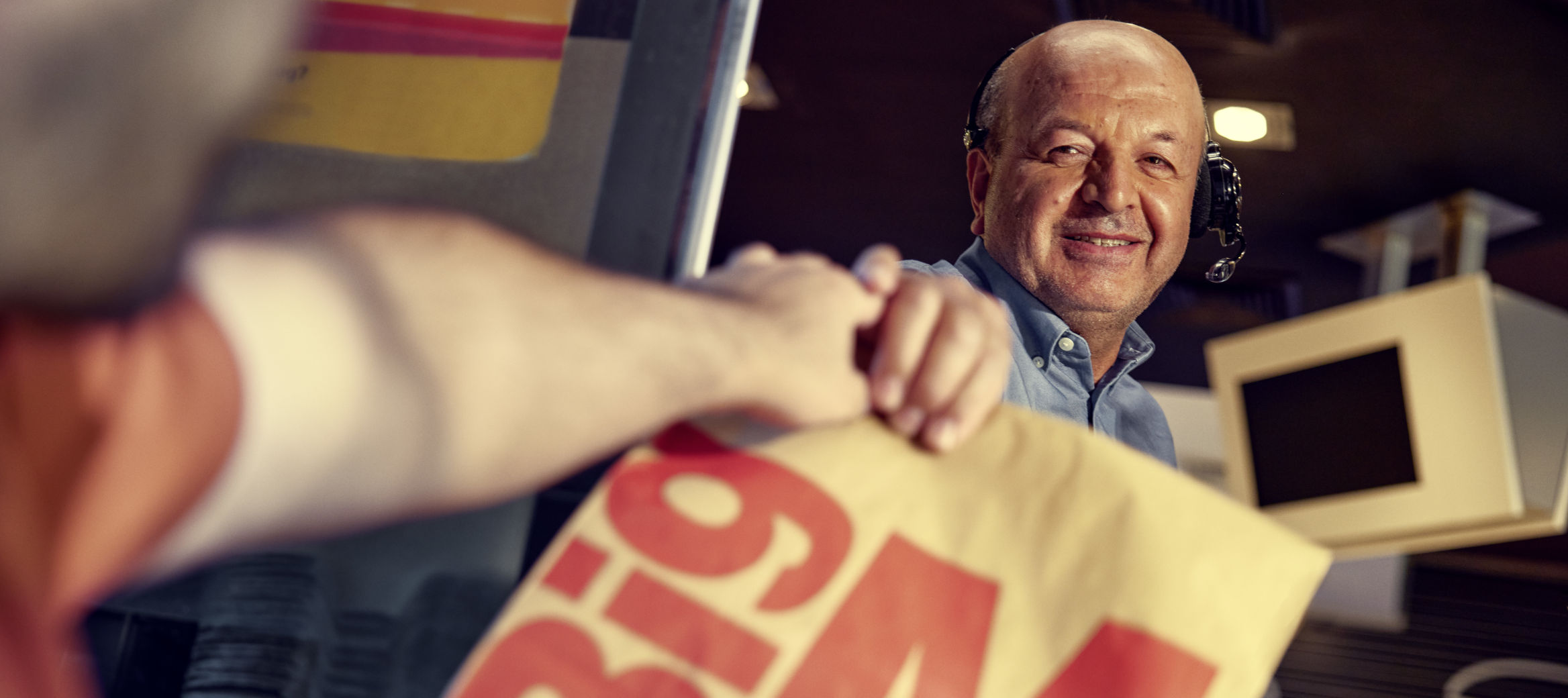 McDonald’s Mitarbeiter am Drive-In Schalter reicht männlichem Kunden seine Außer-Haus-Papiertüte