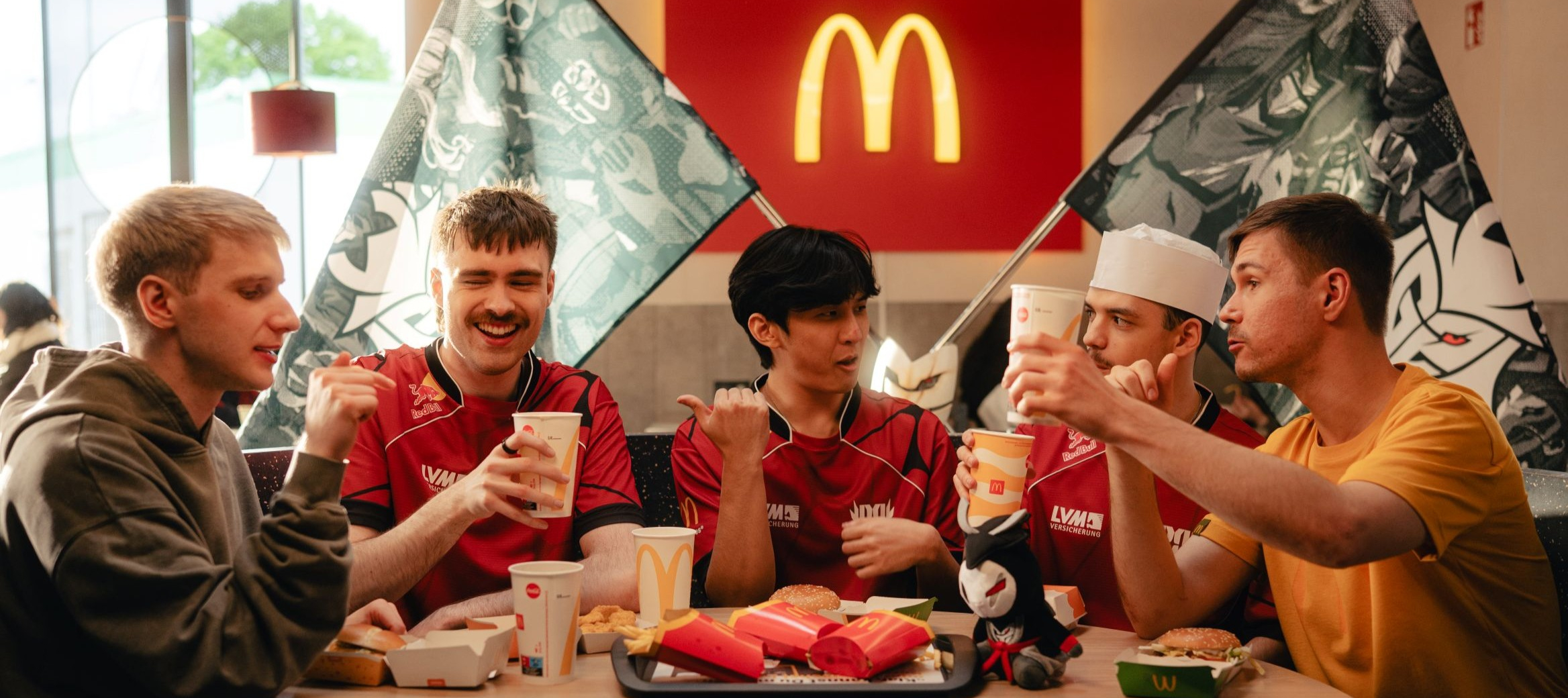 Eine Gruppe junger männlicher Personen speisen an einem Tisch in einem McDonald’s Restaurant und haben gute Laune.