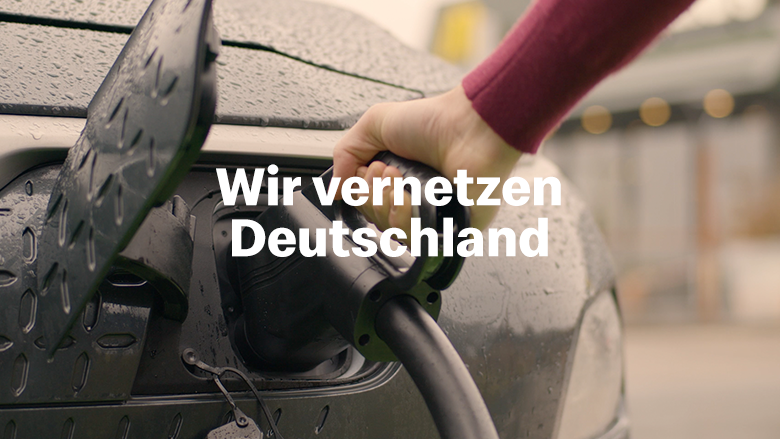 Ladestecker in die Ladebuchse eines E-Autos. Text: Wir vernetzen Deutschland.