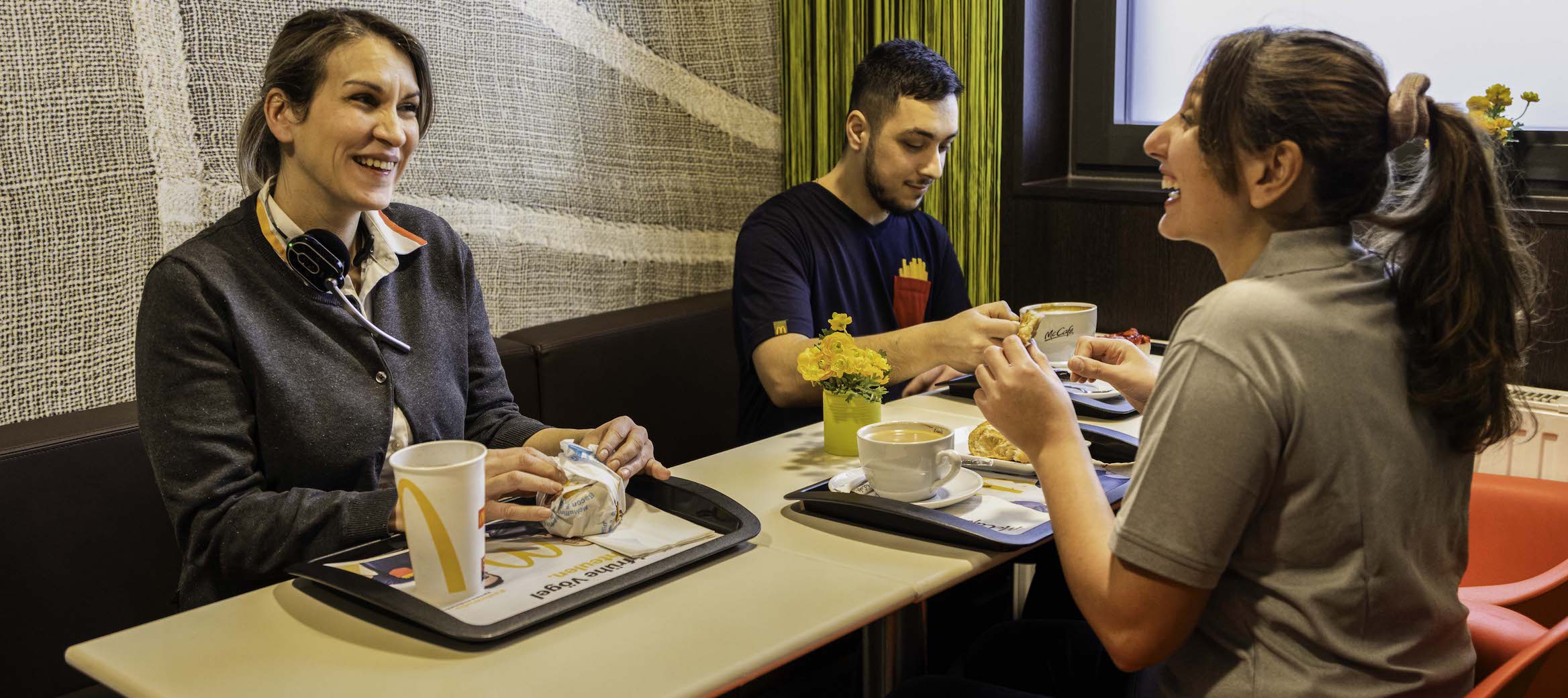 Mehrere Personen sitzen gemeinsam an einem Tisch im McDonald’s-Restaurant, essen und unterhalten sich.
