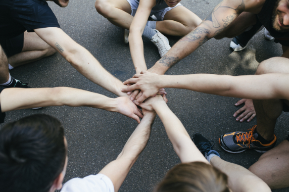 A group of amateur athletes bring their hands together in a show of unity and sportsmanship before playing a friendly game of basketball outdoors.