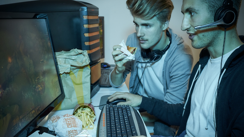 Zwei Gamer schauen gebannt auf einen Computer-Bildschirm und essen dabei McDonald's-Produkte