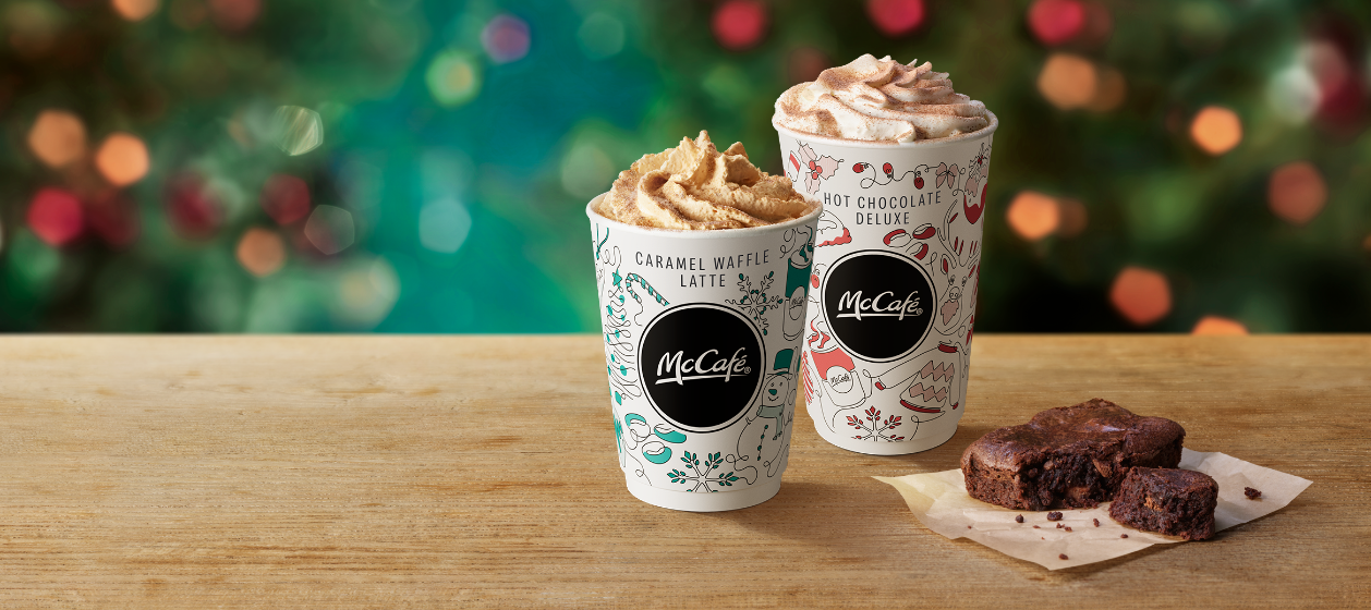 Caramel Waffle Latte, Hot Chocolate Deluxe and a chocolate brownie on a table with a Christmas background.