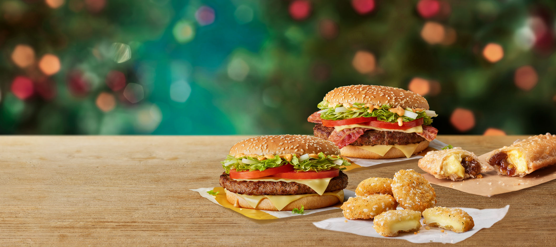 Big Tasty, Big Tasty with Bacon, Cheese Melt Dippers and a Festive Pie on a table with a Christmas background.