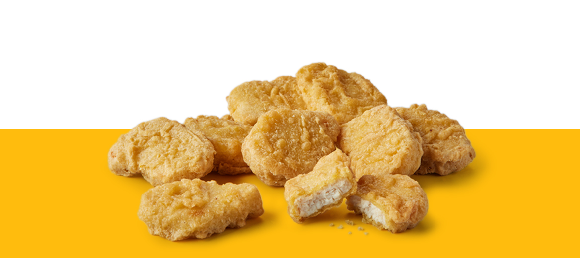 Nine classic chicken McNuggets stacked on a yellow surface against a white background, with one nugget broken open to show the inside.