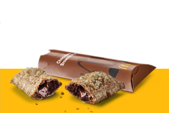 A chocolate filled brownie pie broken open to reveal warm molten filling, placed beside its brown takeaway sleeve.