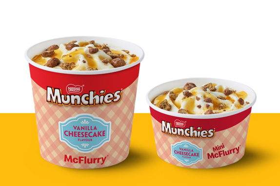 Two McFlurry cups in Munchies Vanilla Cheesecake flavour, topped with caramel drizzle and chocolate-coated pieces.