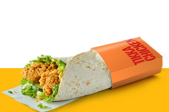 A Tikka Chicken Wrap featuring crispy coated chicken, lettuce and sauce inside a tortilla, partially wrapped in orange packaging.
