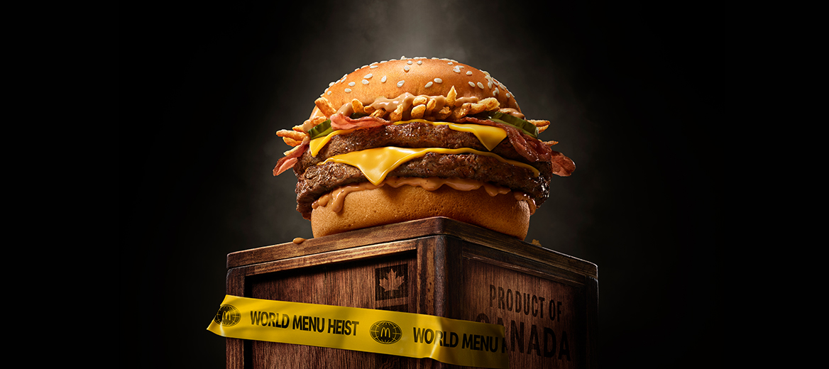 A McDonald’s Maple BBQ & Bacon Double Quarter Pounder™ with Cheese burger displayed on a wooden crate with 'World Menu Heist' tape, featured against dark background. 