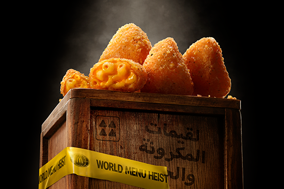 McDonald’s Mac & Cheese Triangles displayed on a wooden crate with 'World Menu Heist' tape, featured against dark background.