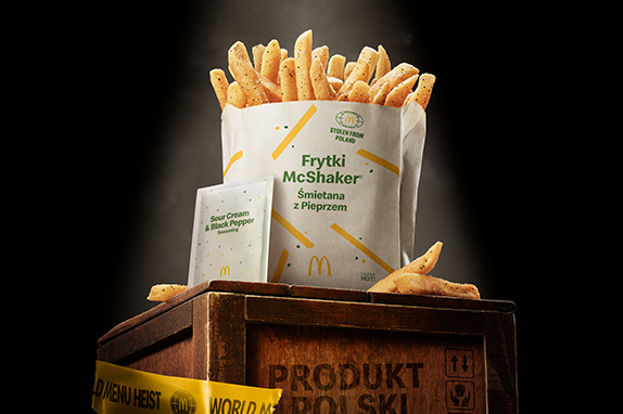 McDonald’s McShaker® Fries seasoned with sour cream and black pepper, served with a seasoning packet, displayed on a wooden crate with 'World Menu Heist' tape, featured against dark background.