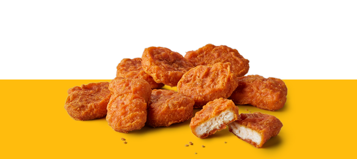 Nine spicy chicken McNuggets stacked on a yellow surface against a white background, with one nugget broken open to show the inside.