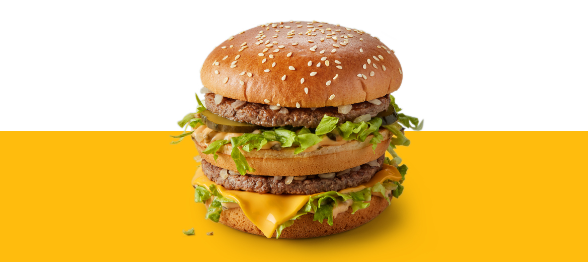 A Big Mac burger with sesame bun, layered beef patties, lettuce, cheese, pickles, and sauce, shown on a yellow surface with a white background.