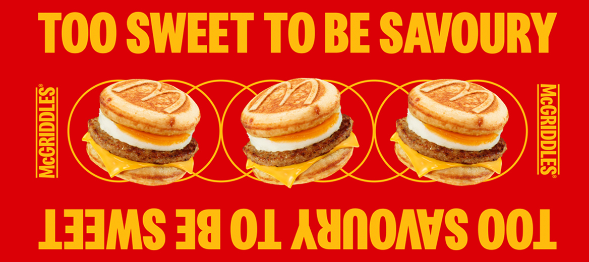 Three sausage and egg McGriddles sandwiches shown in a row on a bright red background, with melted cheese and folded egg visible. Yellow circular graphics surround each sandwich, and the text “Too Sweet to Be Savoury” appears above and below.