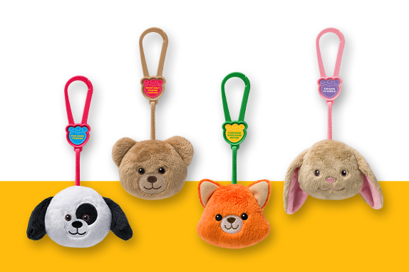 Four Build-A-Bear plush teddy bear heads on a key chain on a yellow shelf 