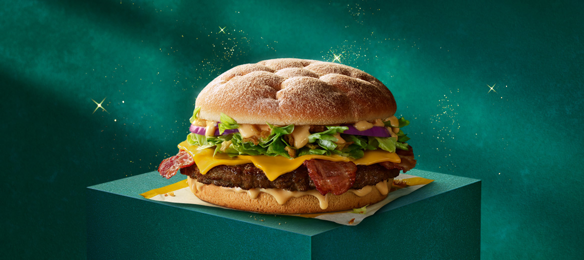 A McDonald’s beef burger with bacon on a green plinth with a green starry background.