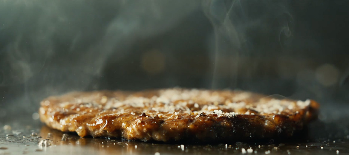 A burger on a grill with onions smoking. 