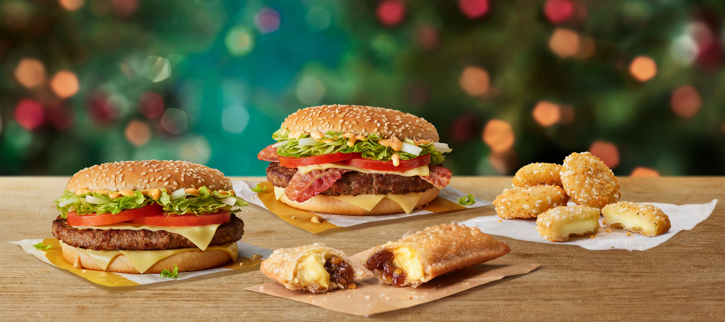 Big Tasty, Big Tasty with Bacon, Cheese Melt Dippers and a Festive Pie on a table with a Christmas background.