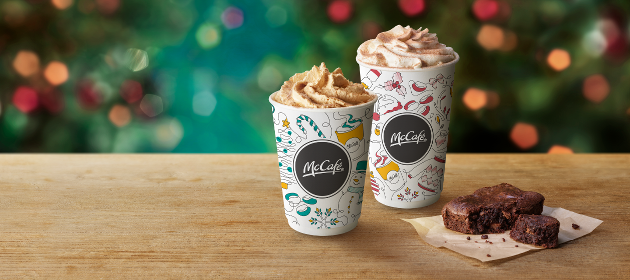 Caramel Waffle Latte, Hot Chocolate Deluxe and a chocolate brownie on a table with a Christmas background.