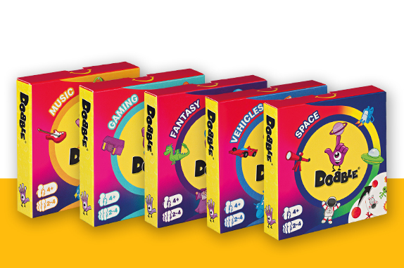 A row of colourful Dobble-themed toy boxes featuring categories such as music, gaming, fantasy, vehicles and space, each decorated with matching symbols.