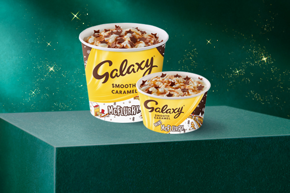 Two caramel McDonald’s yellow ice cream cups on a green plinth with a starry background.
