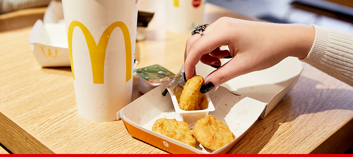 A hand is grabbing some chicken nuggets and dipping in a sauce packet.