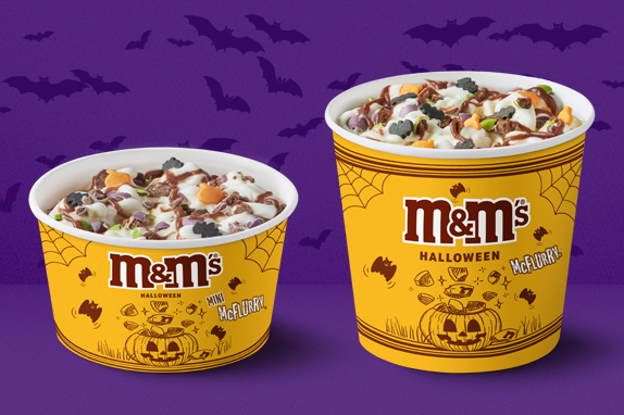 A purple background with bats flying and two McFlurry ice creams on Halloween packaging.