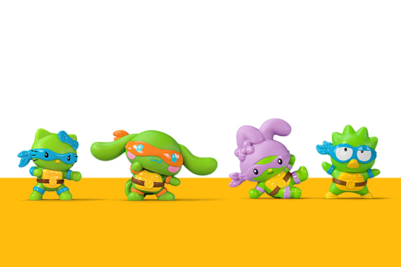 Four colourful toy figures styled as Ninja Turtles and Hello Kitty characters, standing on a yellow surface against a white background.