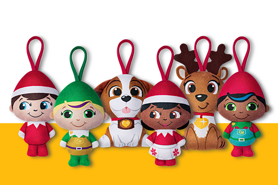  Six plush holiday ornaments in a row: four elves in red and green outfits, a dog, and a reindeer, all with hanging loops.