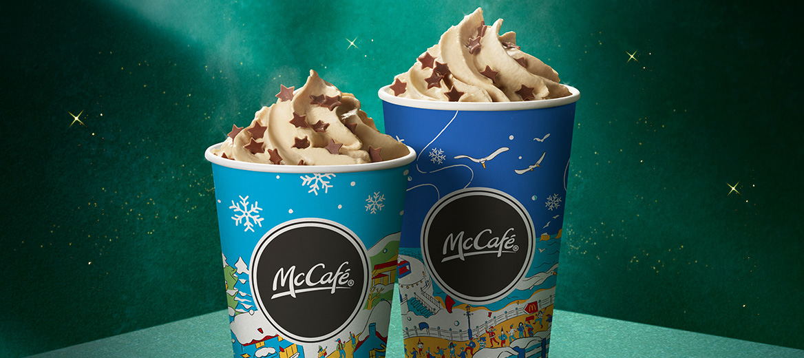 Two McCafé blue cups on a green plinth with a green starry background.