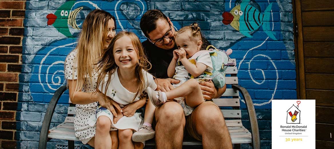 Family sitting on a bench in front of a mural. 