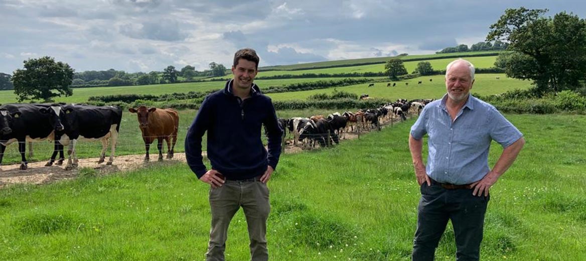 Image of two farmers smiling in a field with a herd of cows in the background.