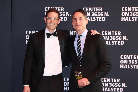 Two men in suits posing for a photo in front of the media wall at the Center on Halsted’s annual spring gala